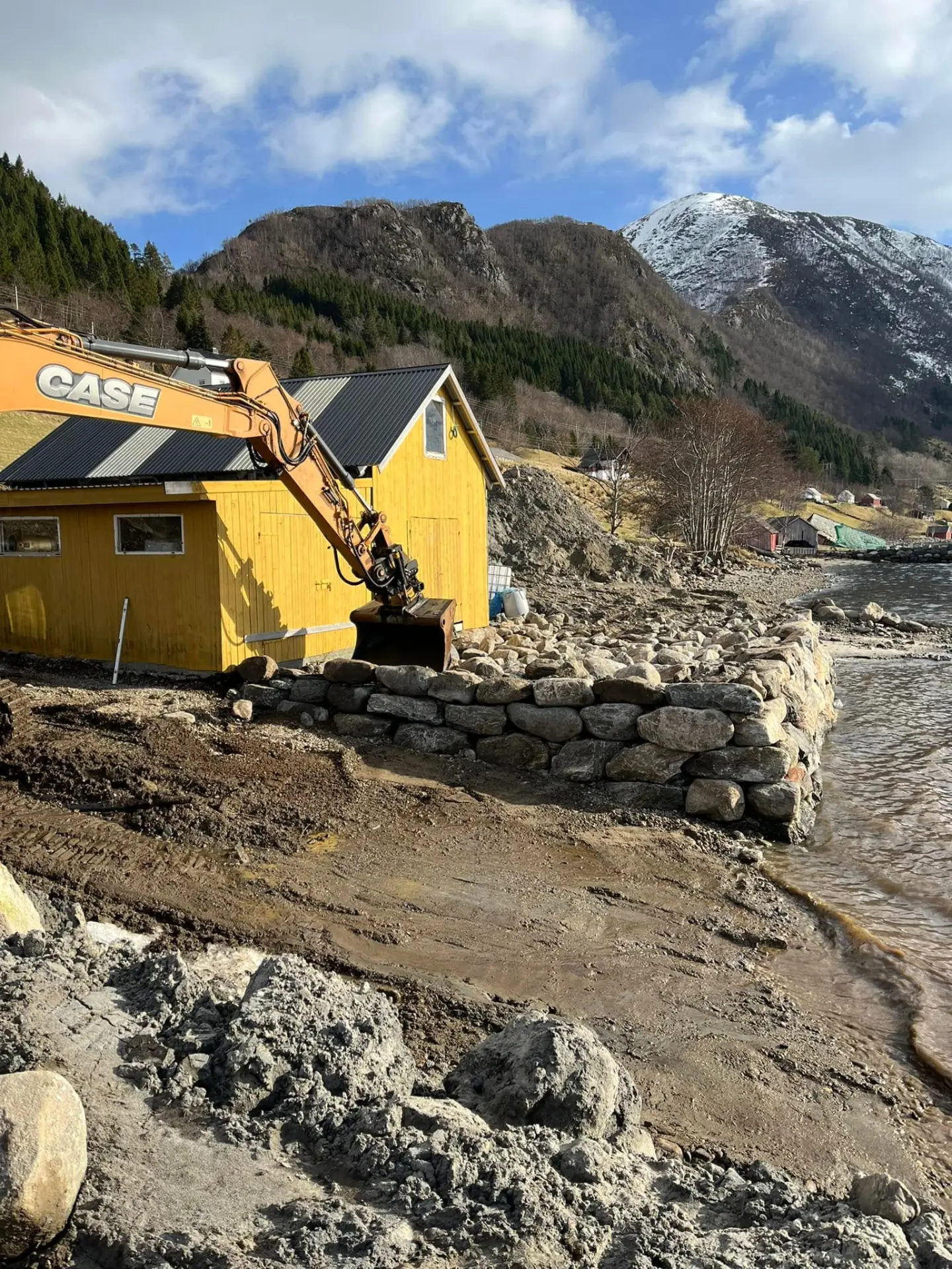 Gravemaskin frå Aasemyr Anleggsservice ved natursteinsmur ved fjorden